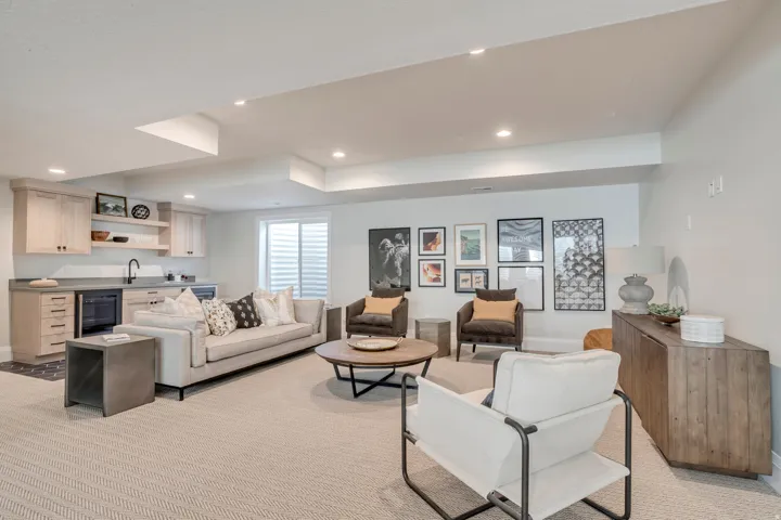 Recessed lighting illuminates this versatile lower-level space featuring a wet bar with light wood cabinetry, a built-in beverage cooler, and a deep basin sink