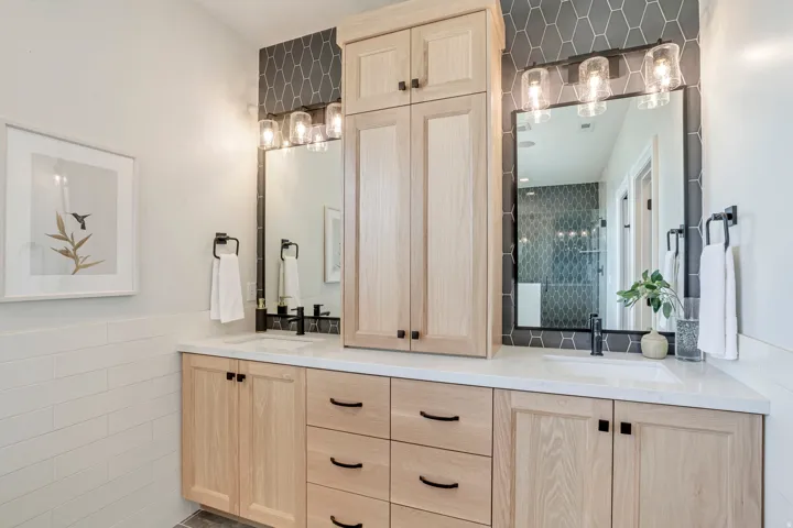 Dual vanity with light wood cabinetry, white countertops, and matte black fixtures