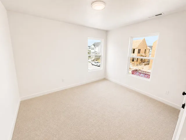 Bright room featuring two windows, neutral carpet, and white walls