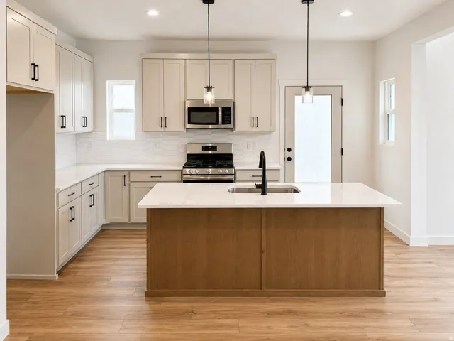 Modern kitchen featuring a central island with an undermount sink and matte black faucet, light wood-finish flooring, white shaker-style cabinetry with black hardware, stainless steel appliances, and white subway tile backsplash