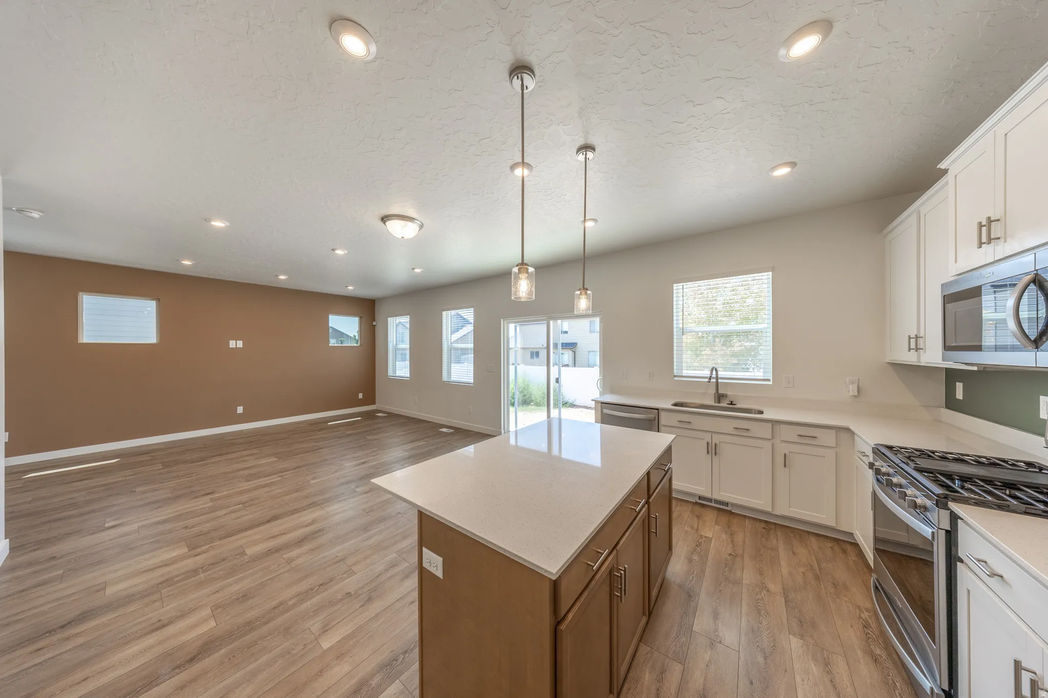 Kitchen featuring white cabinetry, stainless steel appliances, a center island with pendant lighting, and wood-finish flooring