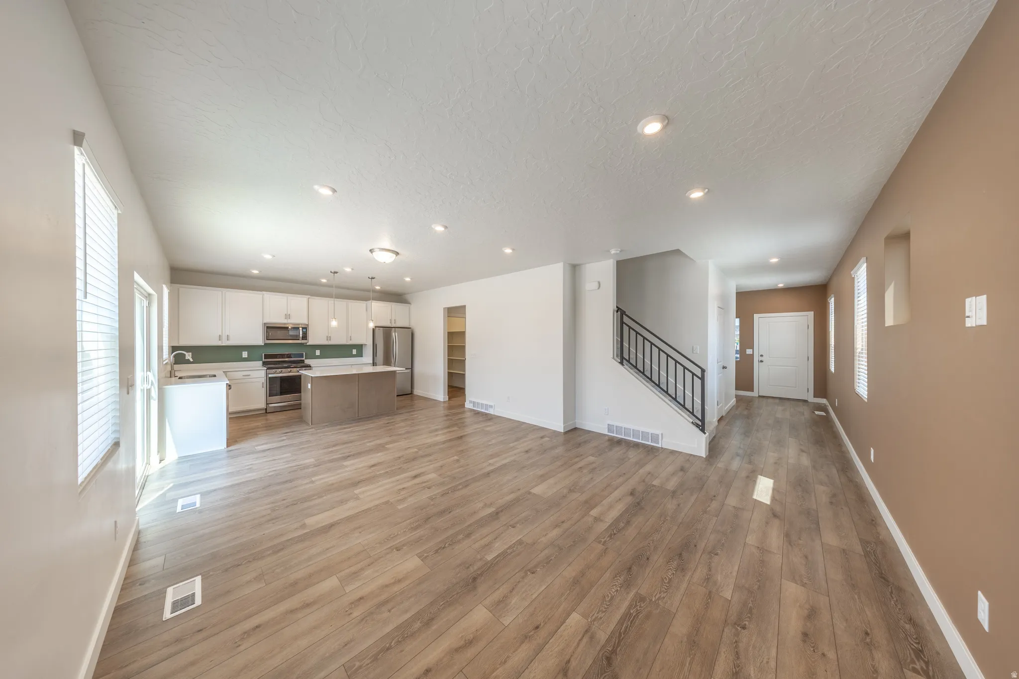 Open-concept layout featuring wood-finish flooring, recessed lighting, a kitchen island, and a staircase with a metal railing