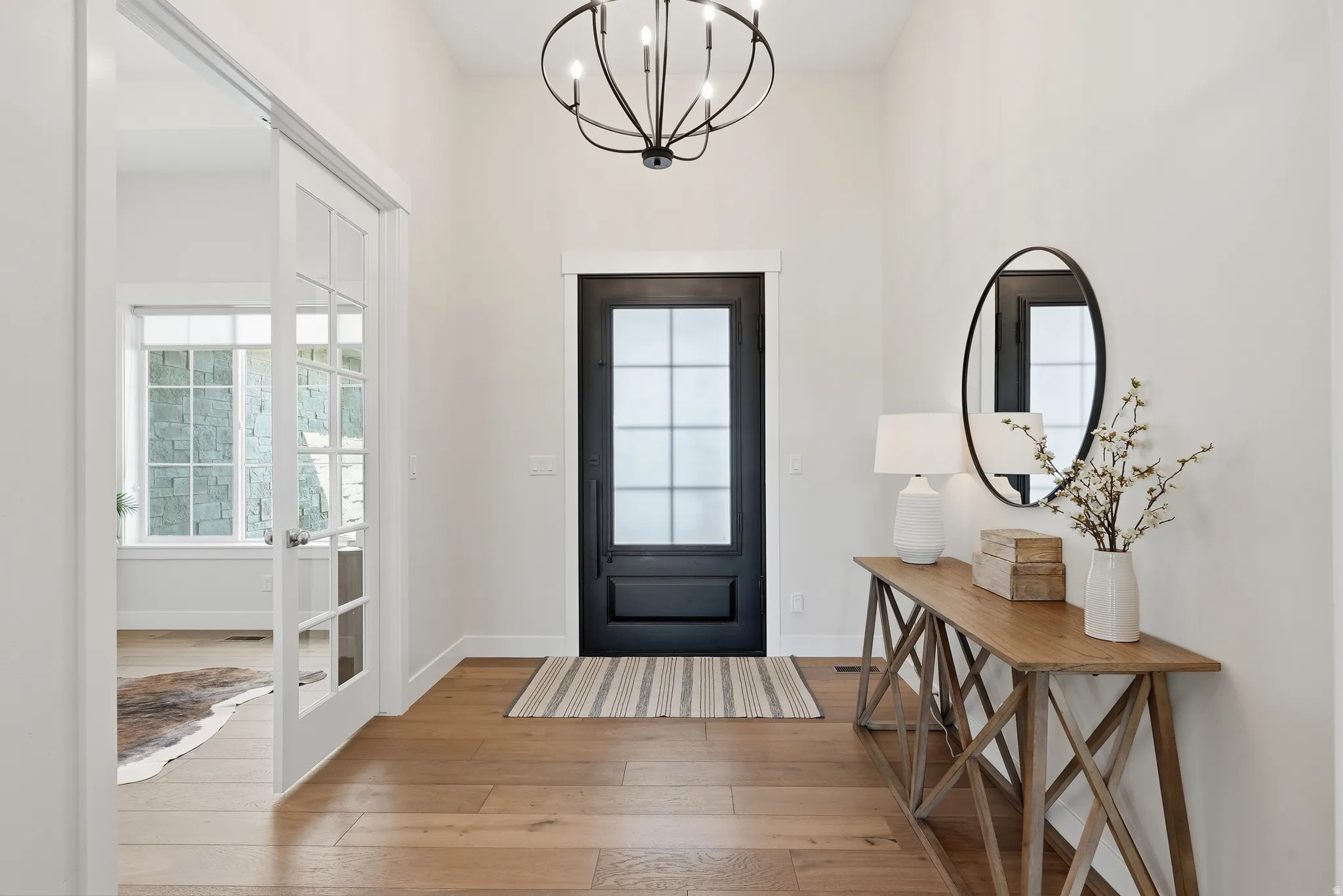 Entryway featuring wood-finish flooring, a black front door with glass panels, and a contemporary chandelier
