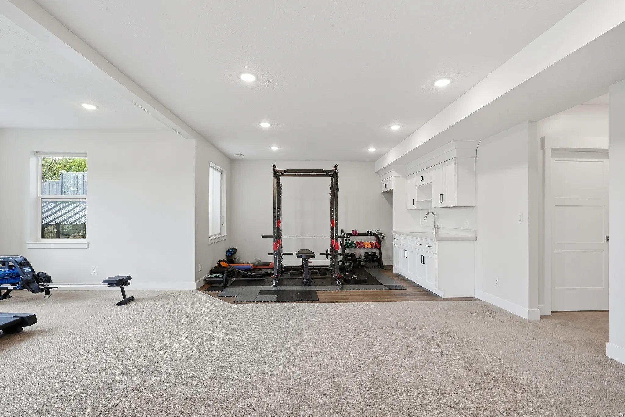 Spacious lower level featuring recessed lighting, light-toned carpeting, and a built-in wet bar with white cabinetry, a sink, and a light-colored countertop