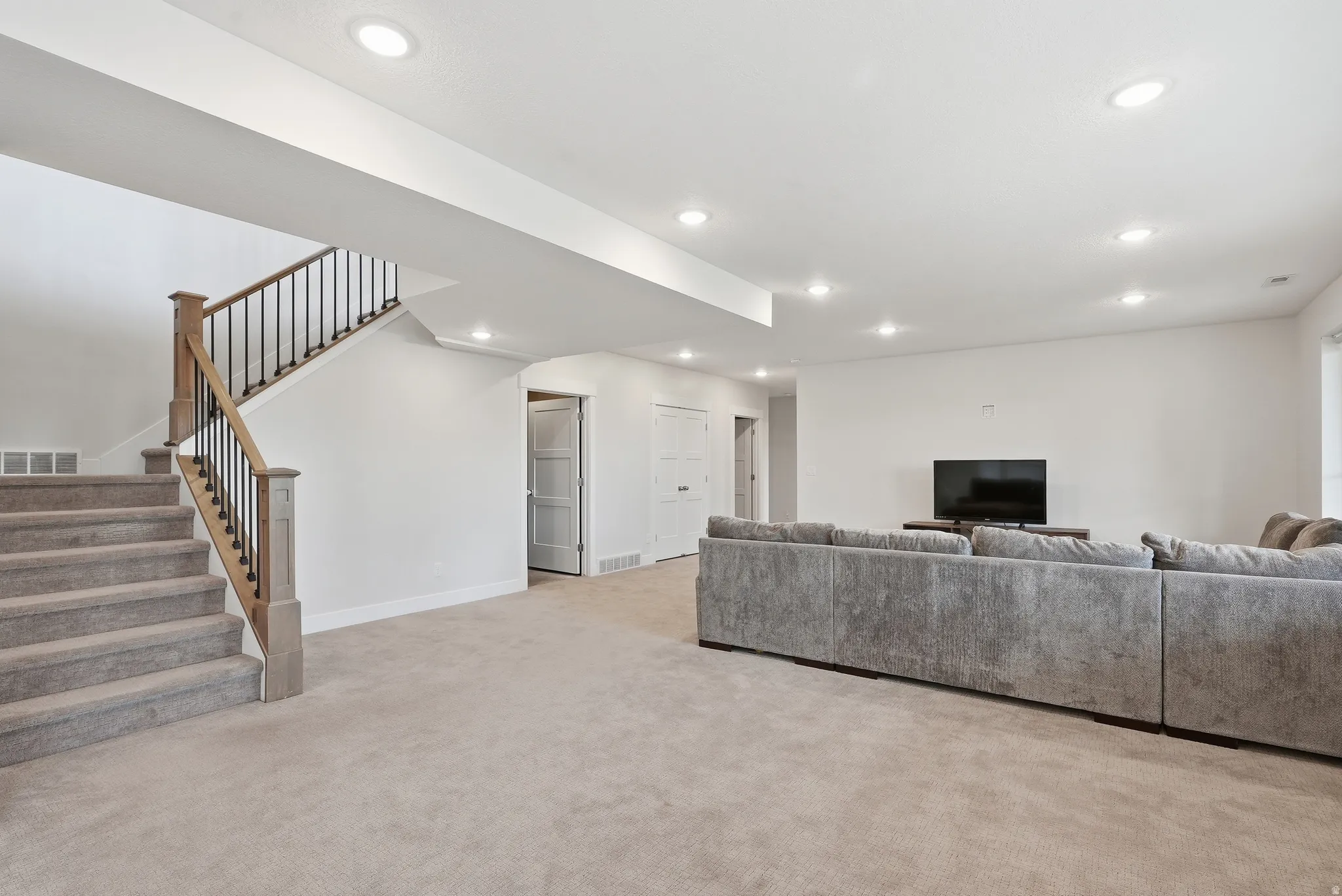 Spacious finished basement featuring recessed lighting, light-toned carpeting, and a staircase with wood newel posts and black metal balusters