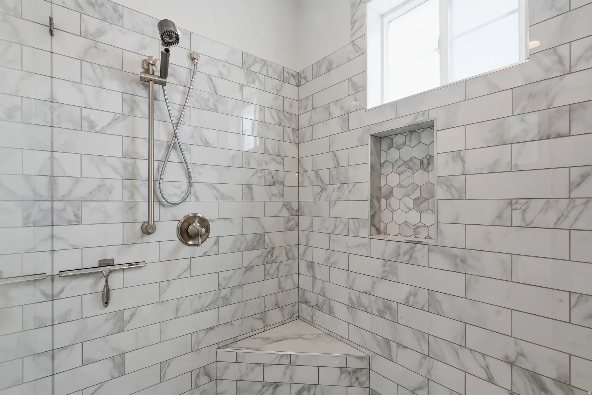 Shower stall featuring subway-style tile with subtle veining, brushed nickel fixtures, a built-in corner bench, a recessed niche with hexagonal tile, and a high-set window