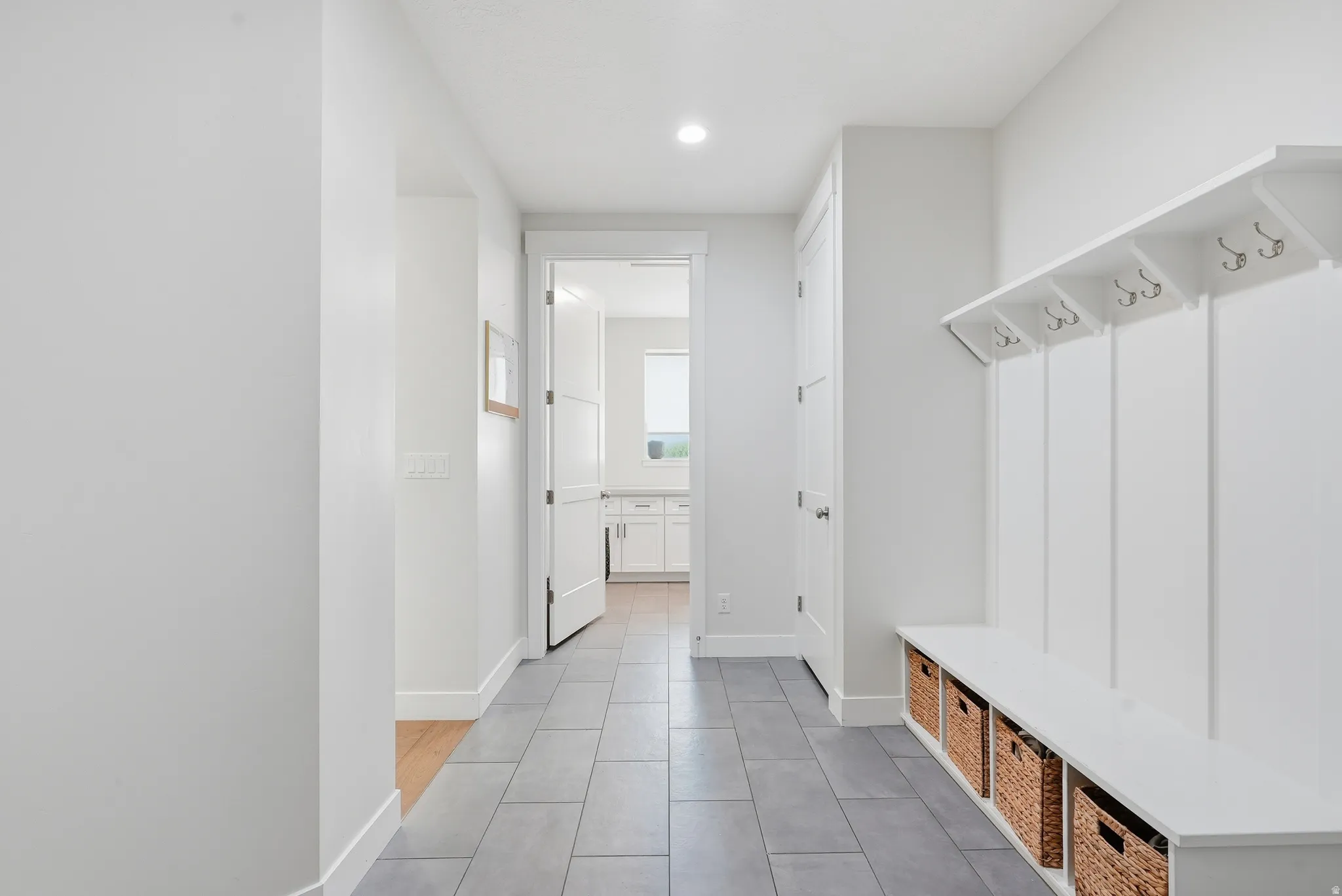 Entryway featuring gray tile flooring, a built-in bench with storage nooks, coat hooks, and recessed lighting