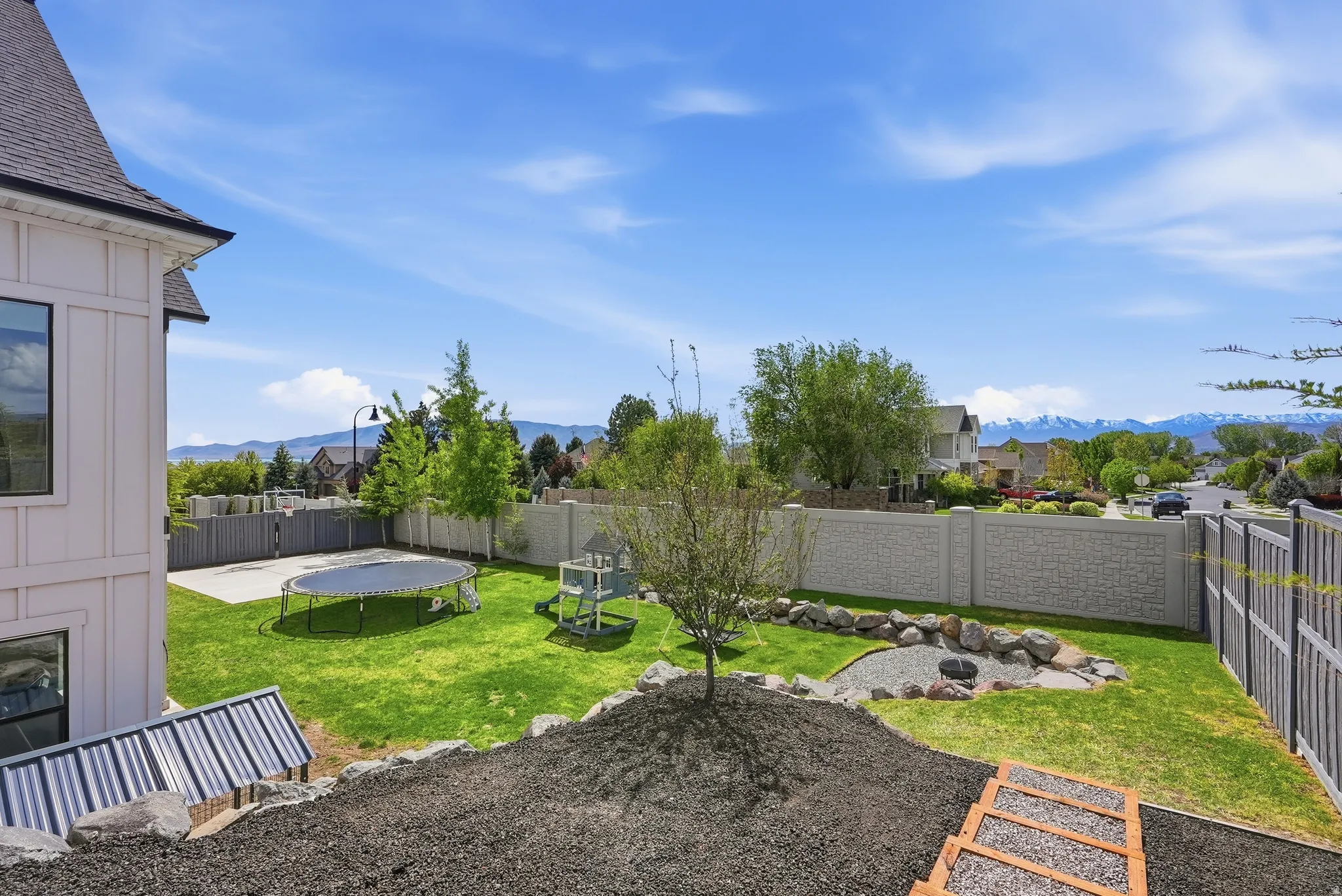 Expansive backyard featuring a manicured lawn, concrete patio, and a stone-edged fire pit area