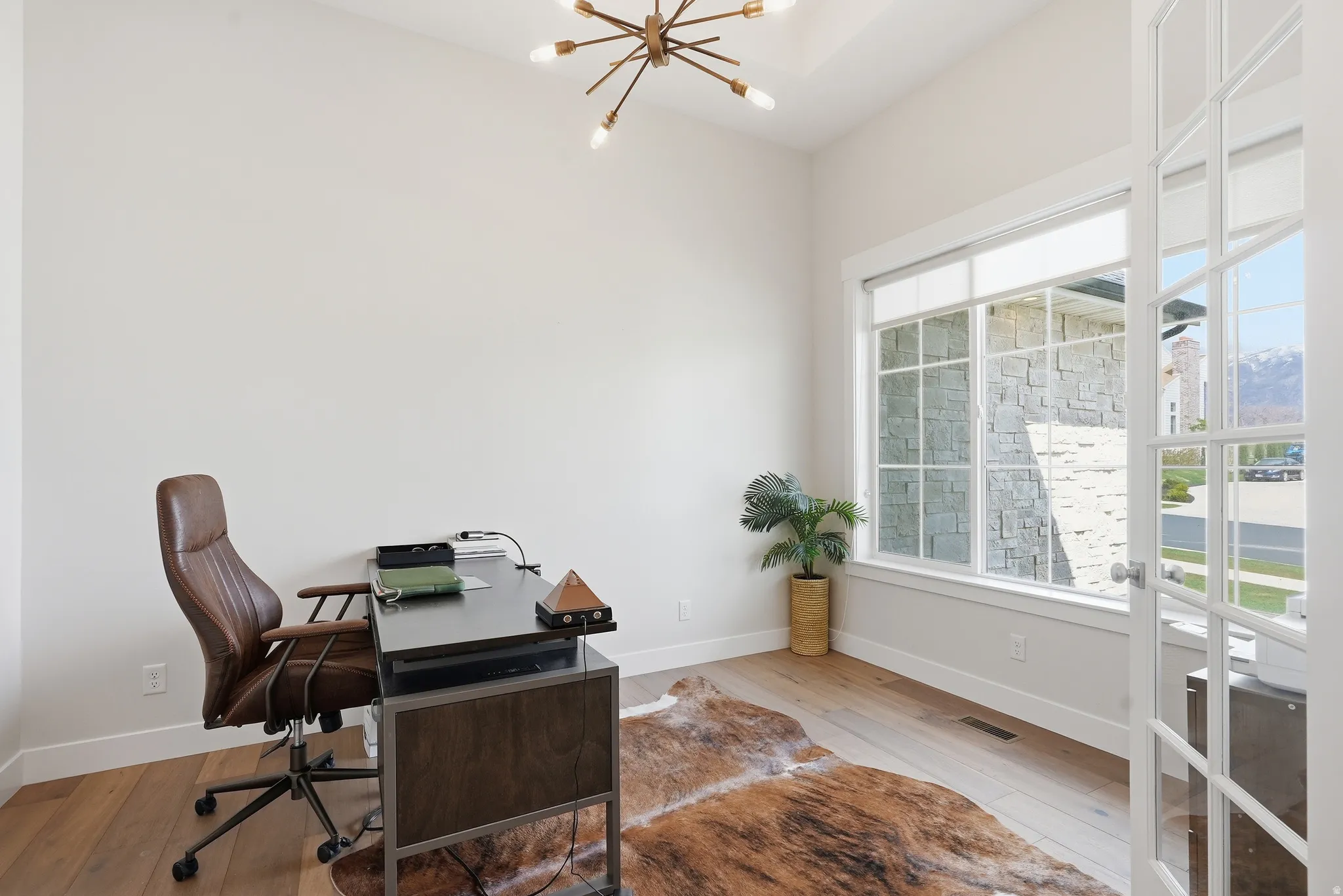 Room featuring light wood-finish flooring, a contemporary sputnik chandelier, and a large window with white grilles