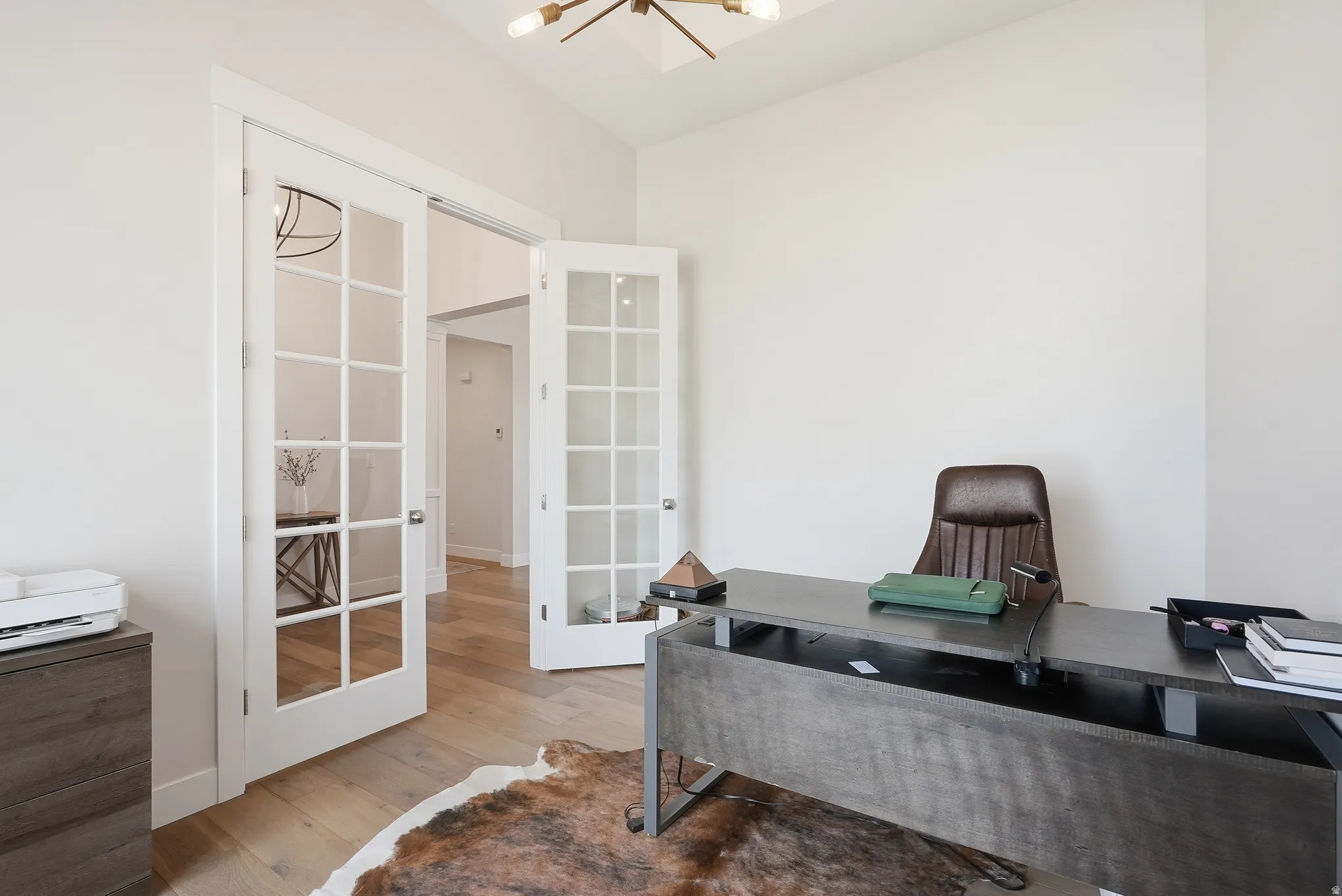 White French doors with multiple glass panes open into a room featuring wood-finish flooring and light-toned walls