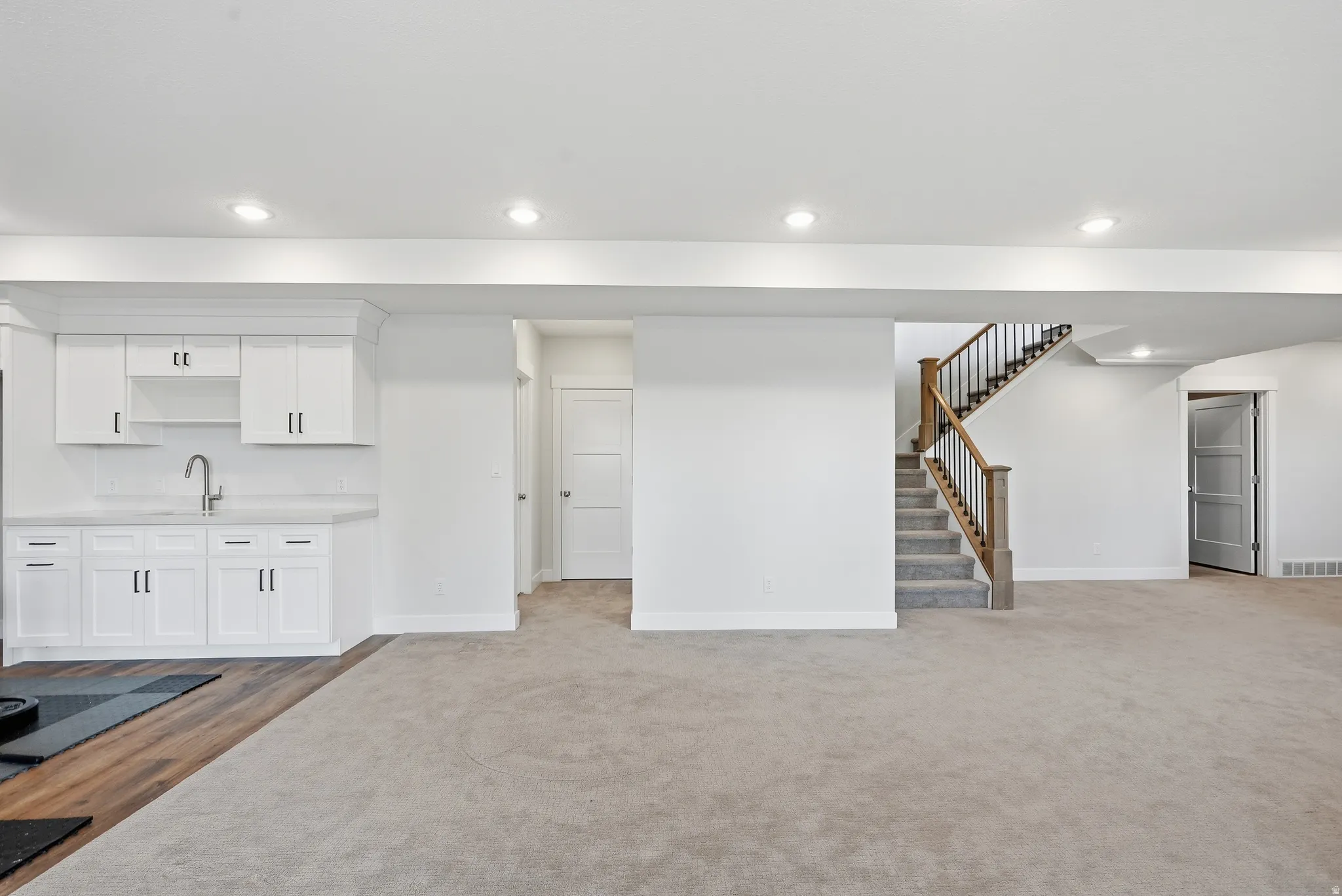 Spacious lower-level area featuring a wet bar with white shaker cabinetry, an undermount sink, and a light-toned countertop