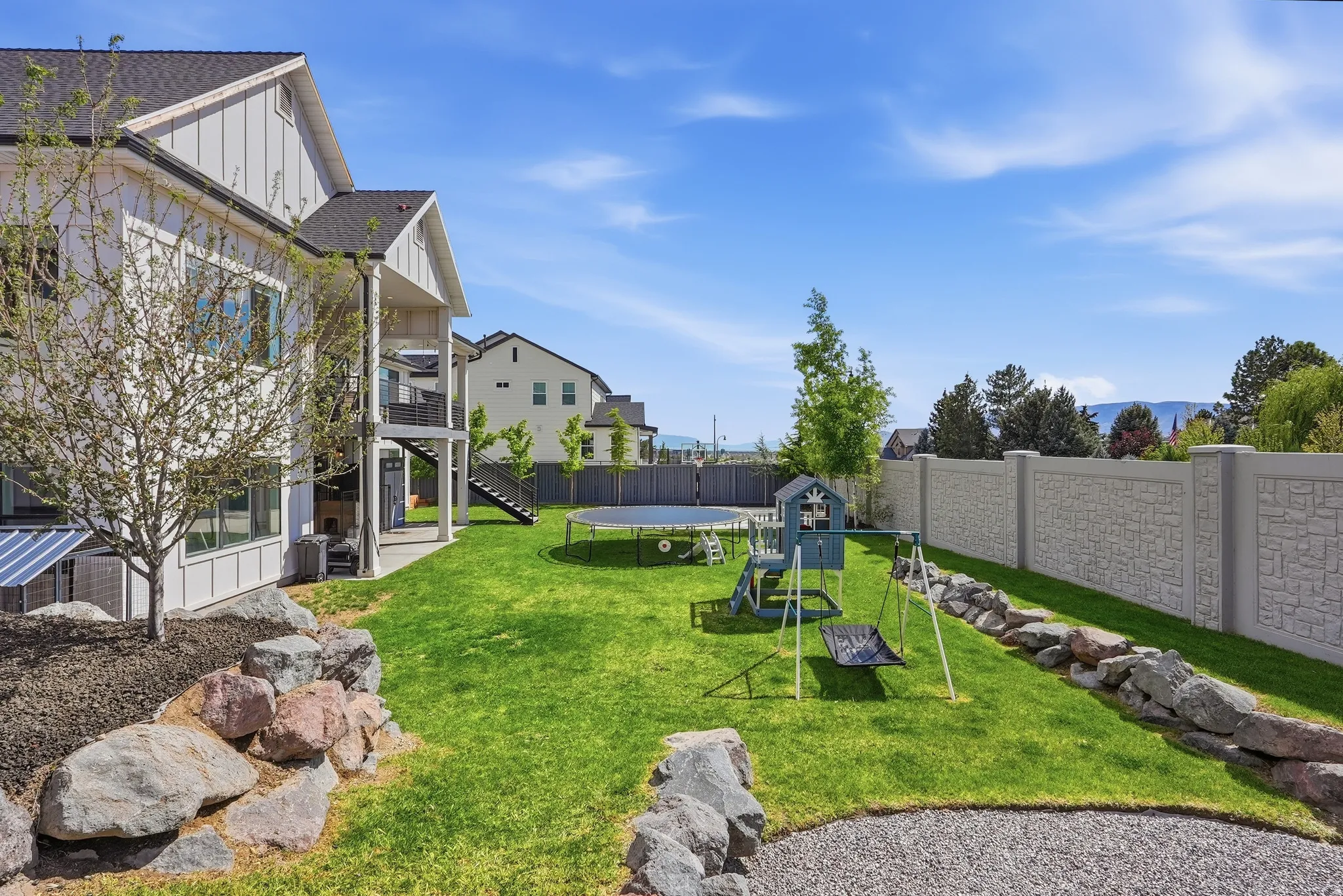 Expansive backyard featuring a lush green lawn, tiered rock landscaping, and a textured privacy fence