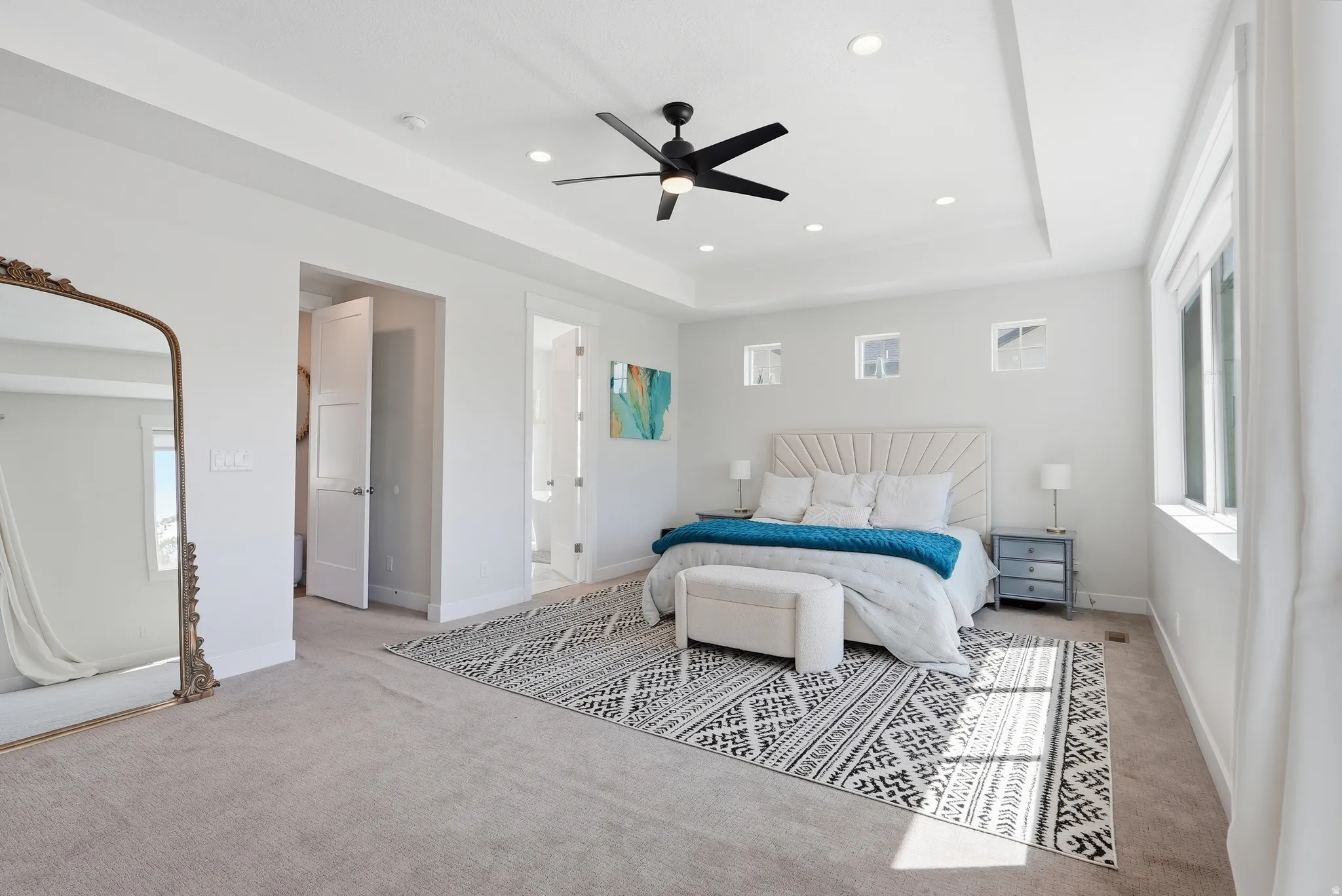 Spacious bedroom featuring a tray ceiling with recessed lighting and a black ceiling fan, multiple windows for natural light, and plush carpet flooring