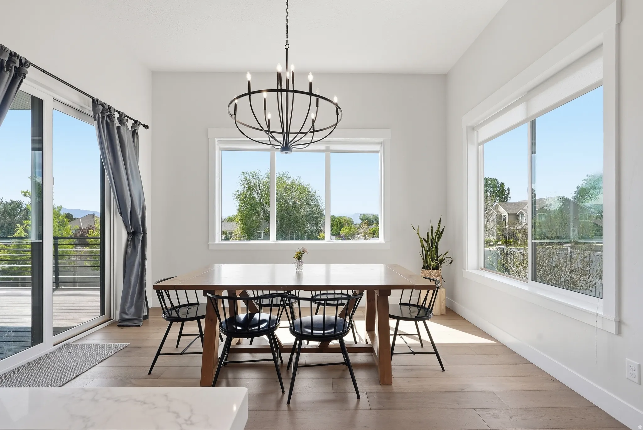 Dining area featuring wood-finish flooring, a large sliding glass door, a contemporary black chandelier, and multiple windows with white trim