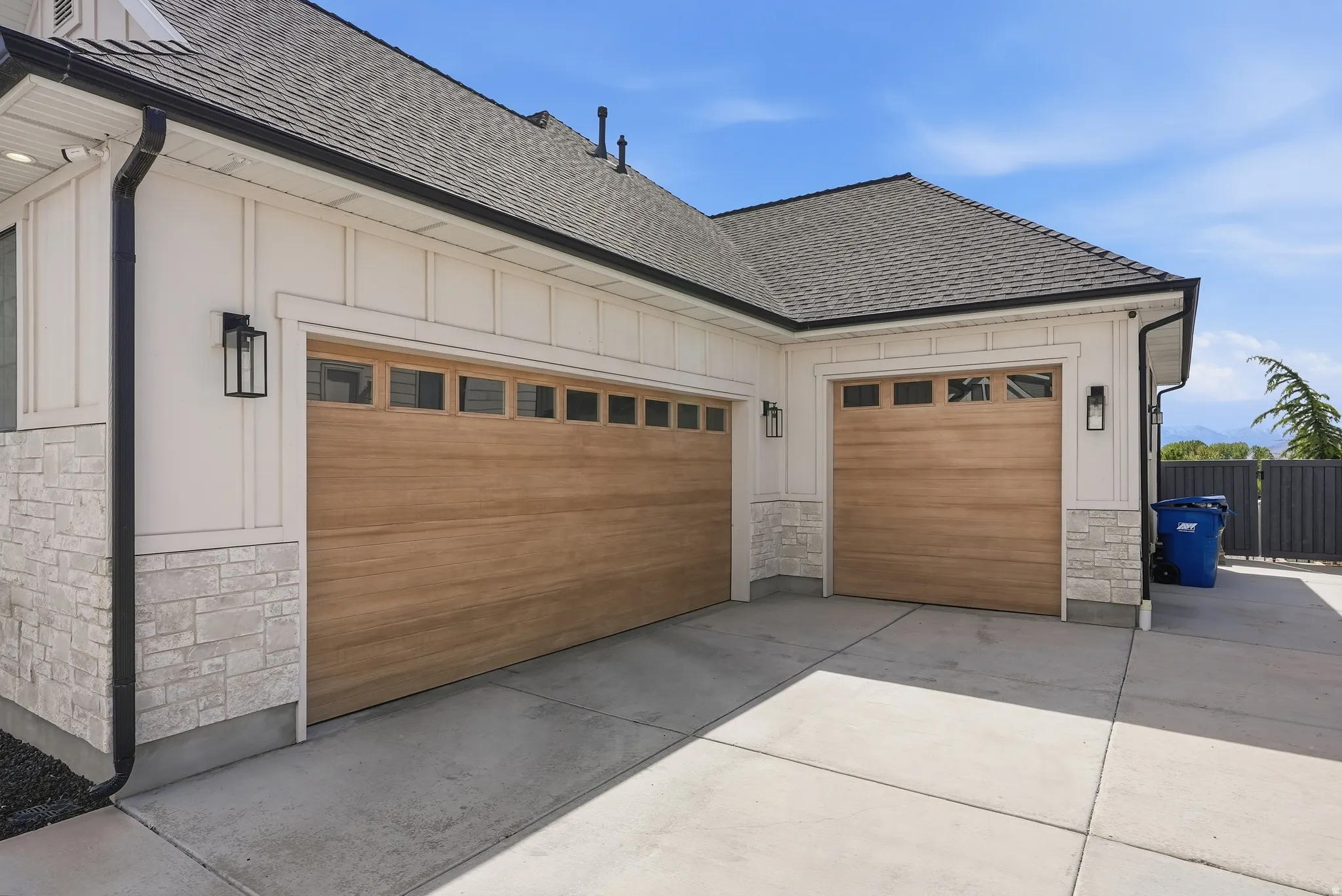 Two wood-finish garage doors with upper window panels, complemented by board and batten siding and a stone facade