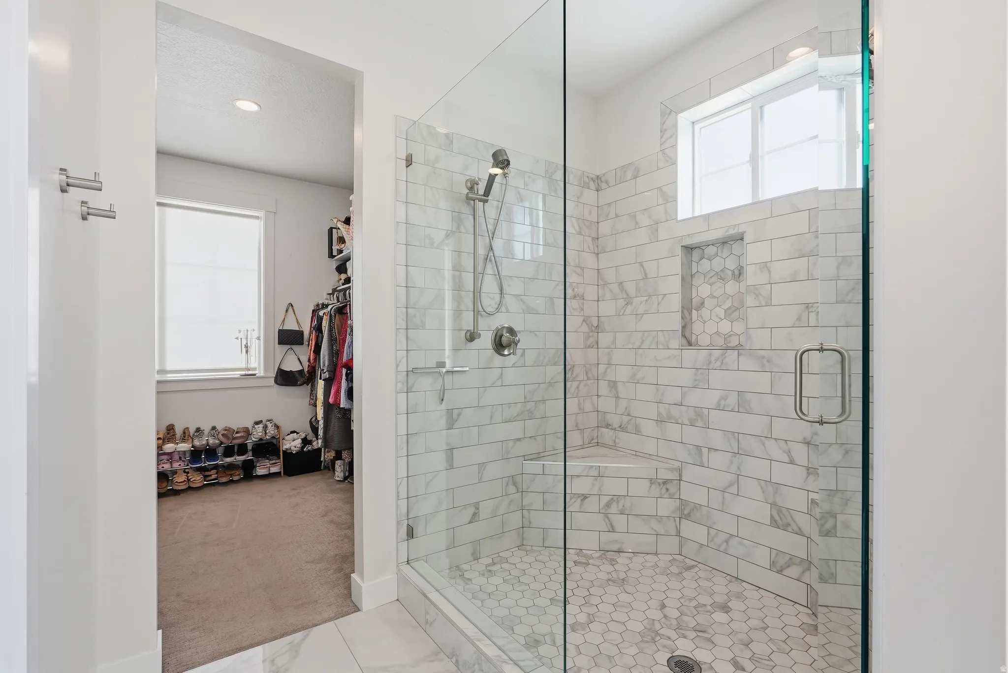 Spacious walk-in shower featuring a glass enclosure, white subway tile walls, a built-in bench, and a recessed niche with hexagonal tile