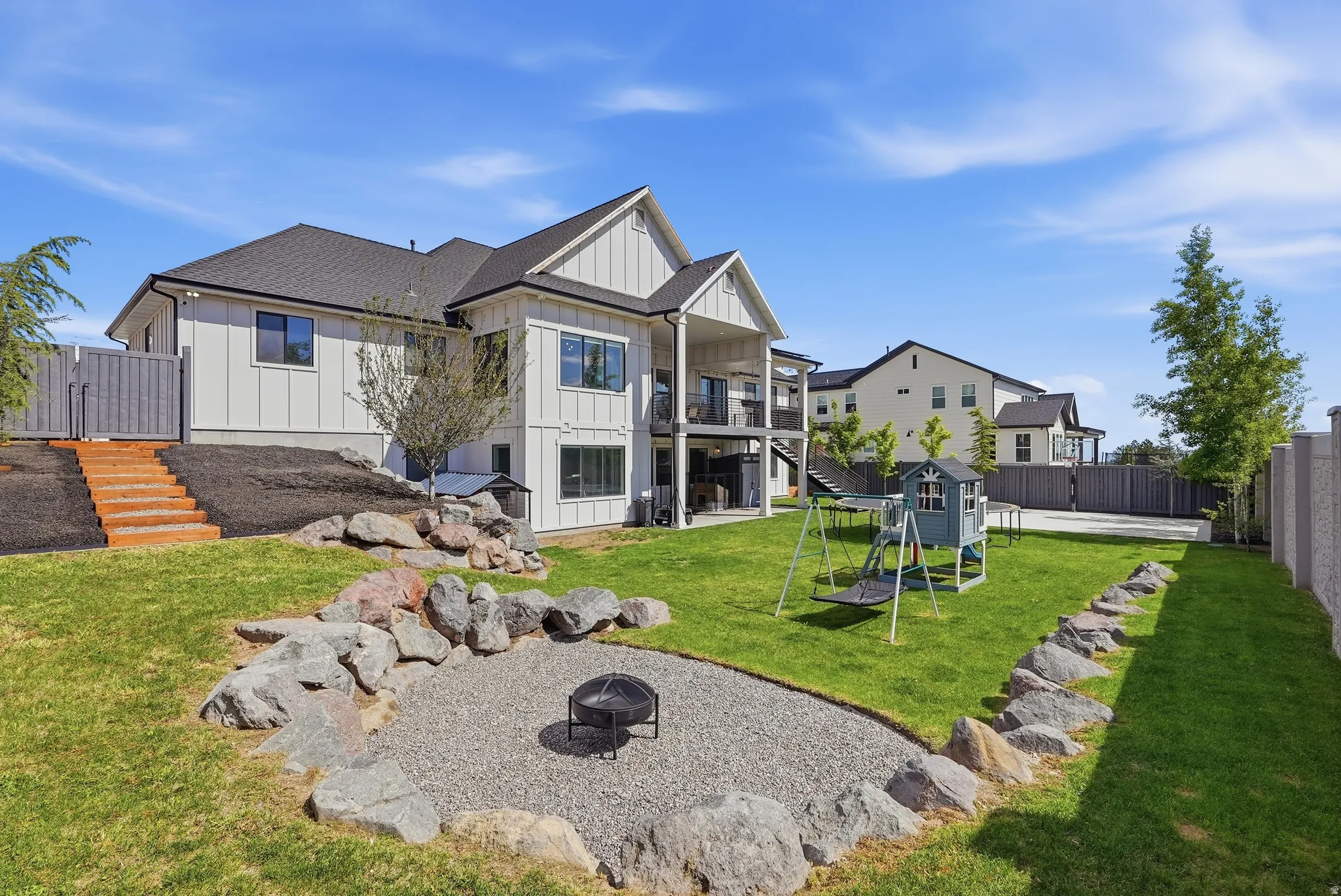 Expansive backyard featuring a lush lawn, a stone-lined fire pit area, and natural wood steps