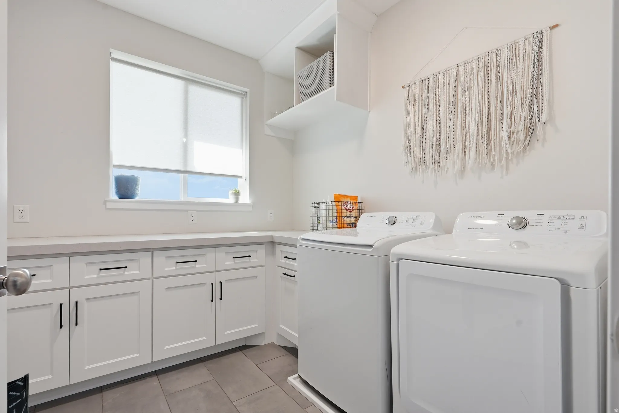 Laundry room featuring white cabinetry, light-toned countertops, a window, and gray tile flooring