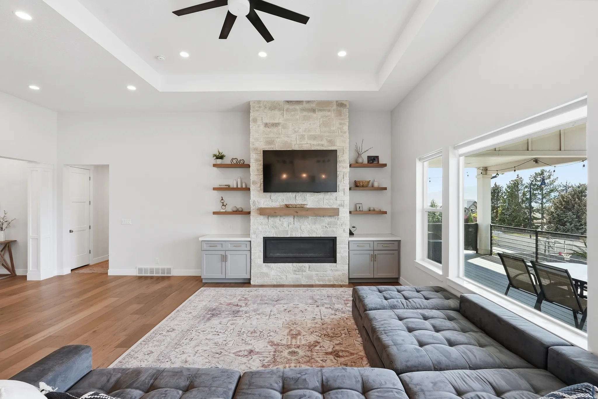 Spacious living area featuring a stone fireplace surround, wood-finish flooring, and a tray ceiling with recessed lighting