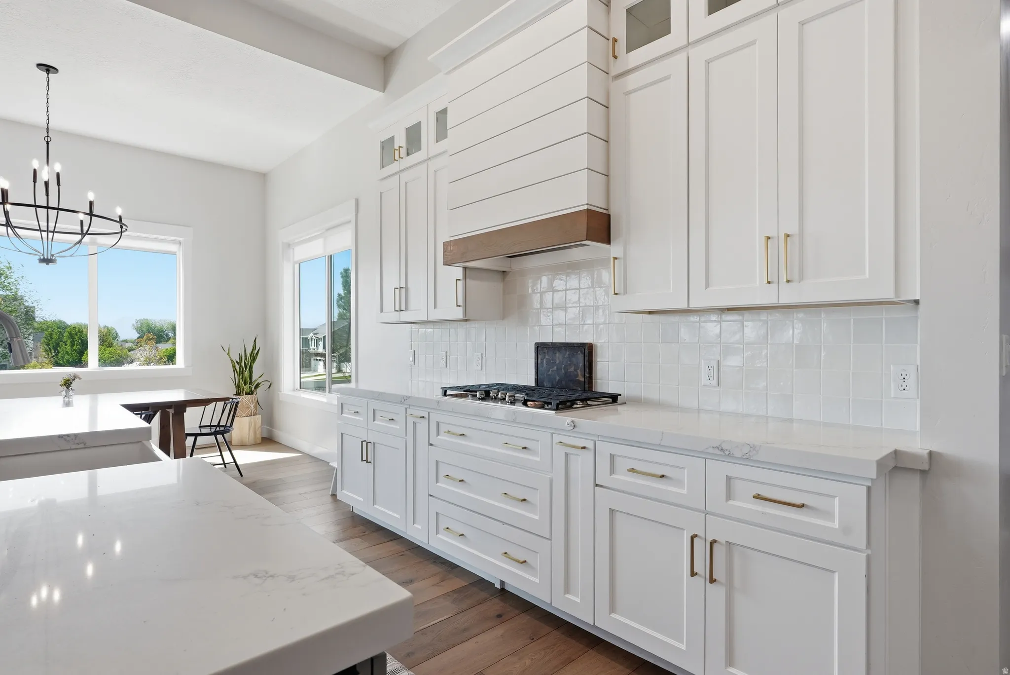 Bright kitchen featuring white shaker cabinetry, light-toned countertops, a gas range with an architectural range hood, a white tile backsplash, and wood-finish flooring