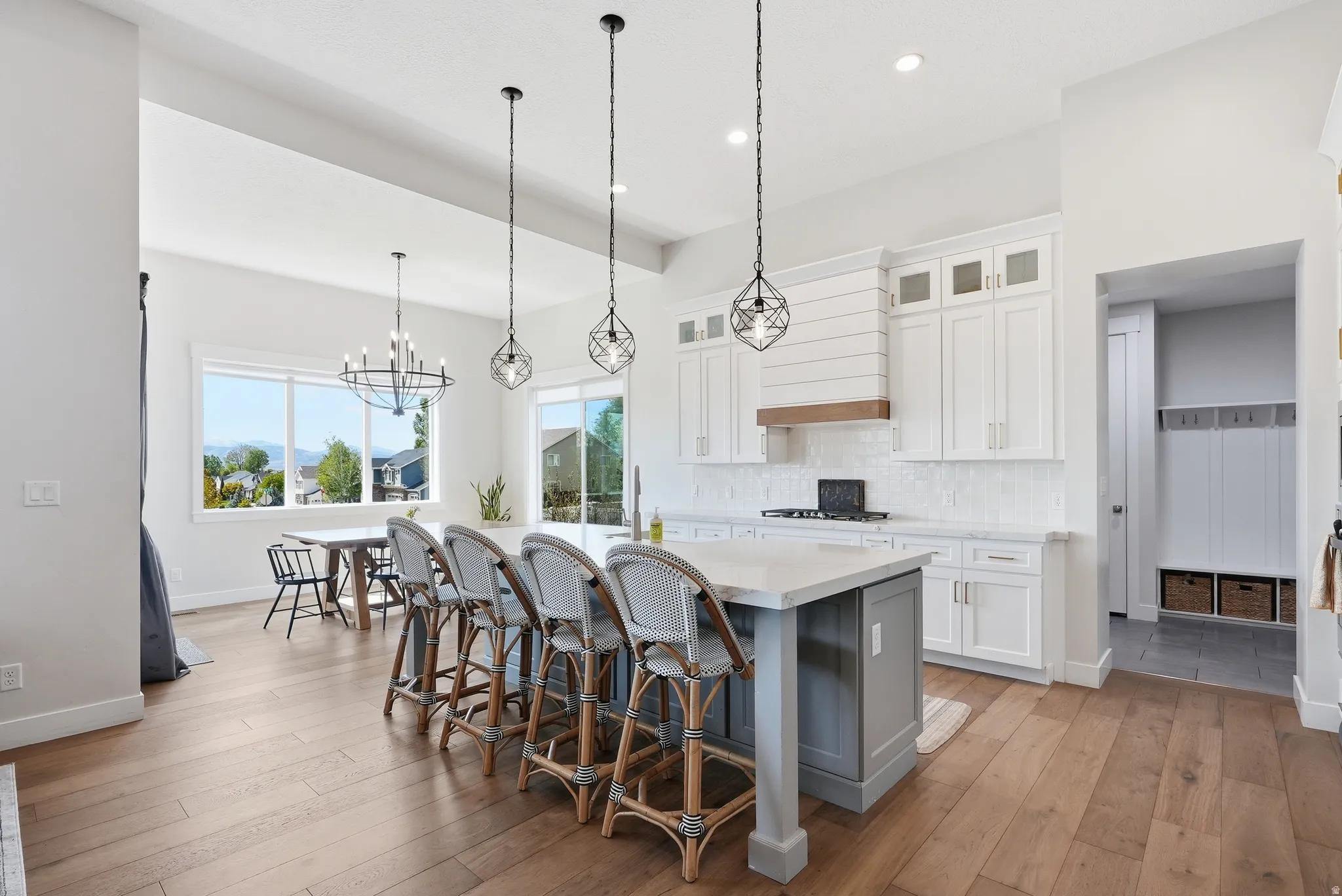 Open-concept kitchen featuring a large central island with seating, a white subway tile backsplash, white shaker-style cabinetry, and wood-finish flooring