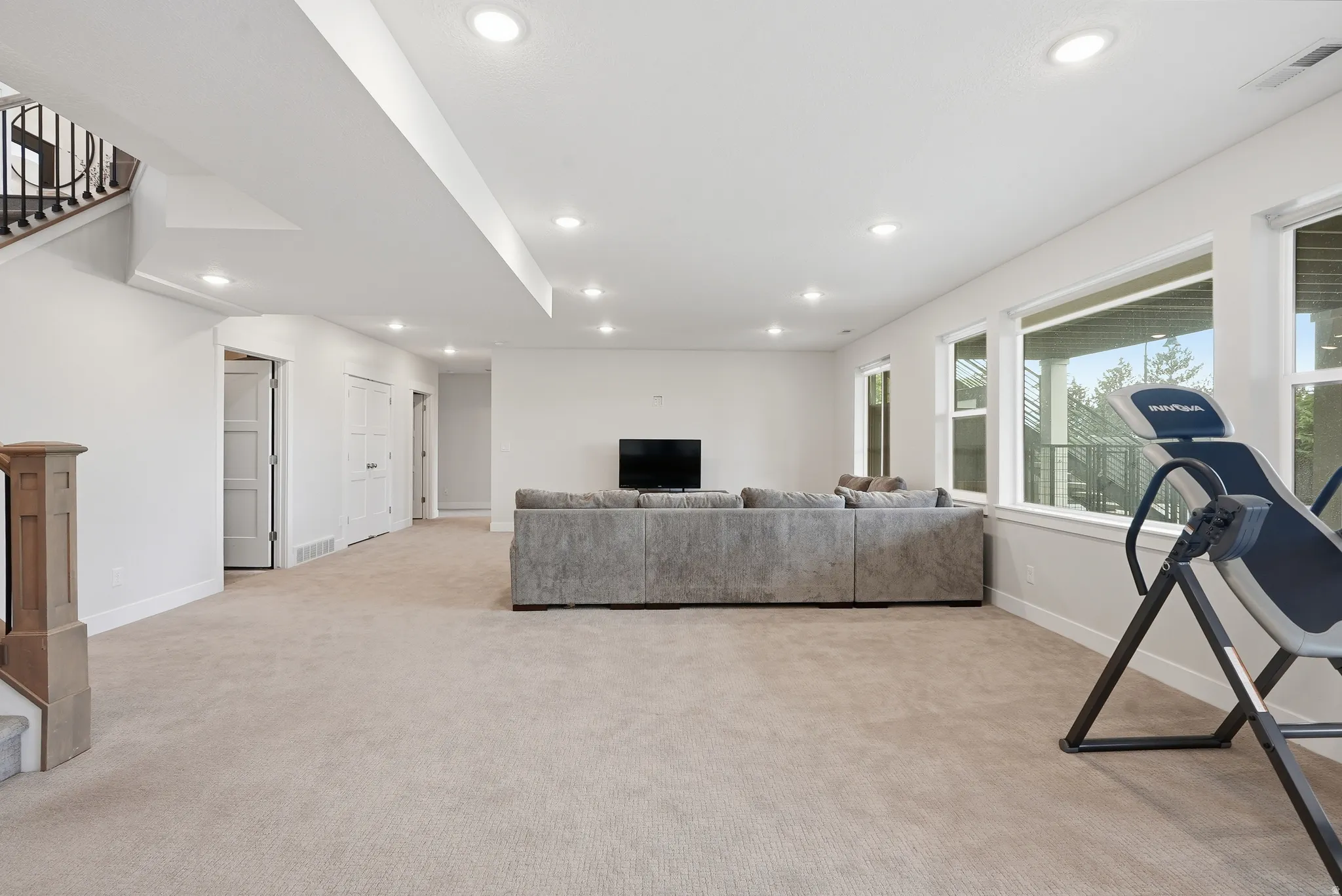 Spacious lower-level room featuring recessed lighting, plush carpet, multiple windows, and a staircase with an open baluster