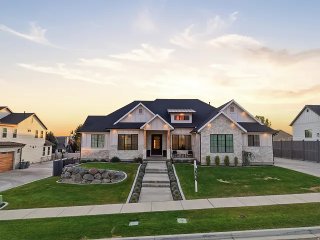 Contemporary residence featuring a stone and board-and-batten facade, dark-framed windows, a prominent entryway, and a landscaped front yard with a rock retaining wall and manicured lawn