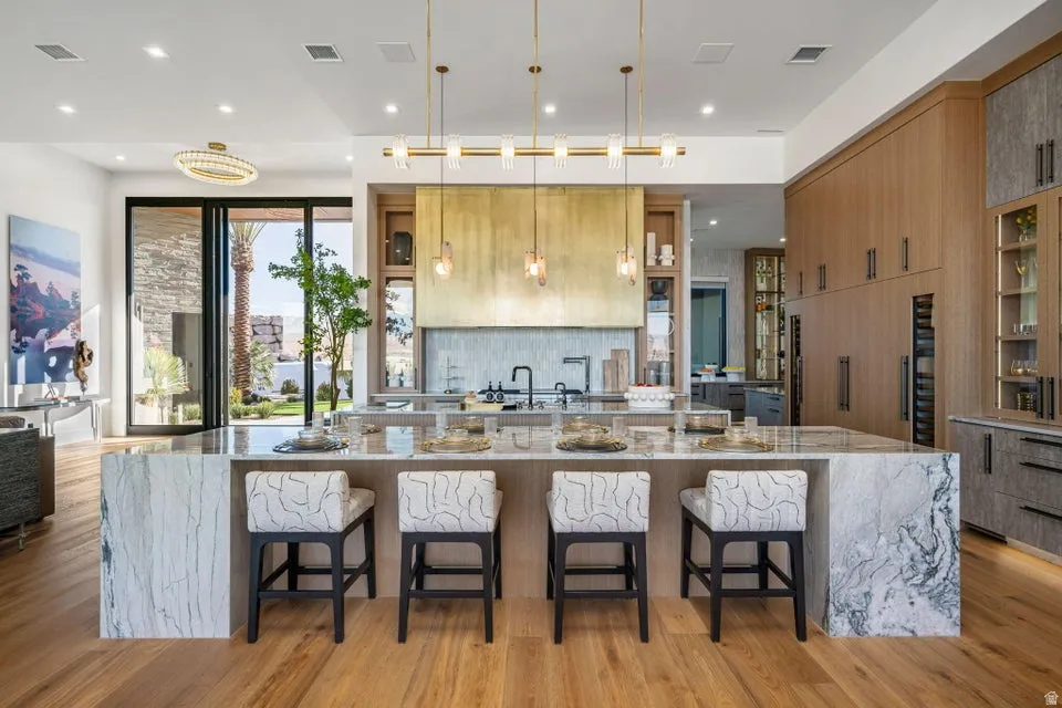Gourmet kitchen featuring a waterfall island, custom wood cabinetry, stainless steel appliances, and wood-finish flooring