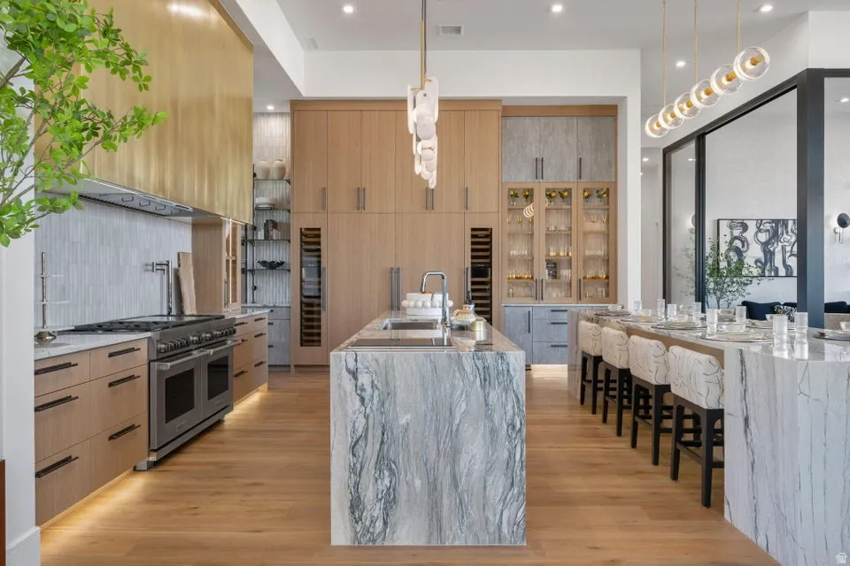 Gourmet kitchen featuring a large waterfall island with integrated sink, a second waterfall island with seating, a professional-grade range, full-height custom cabinetry, and wood-finish flooring
