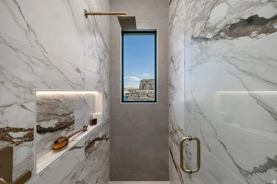 Shower featuring large format marble-look tile walls, a built-in recessed niche with accent lighting, and a rainfall showerhead with a gold-tone finish