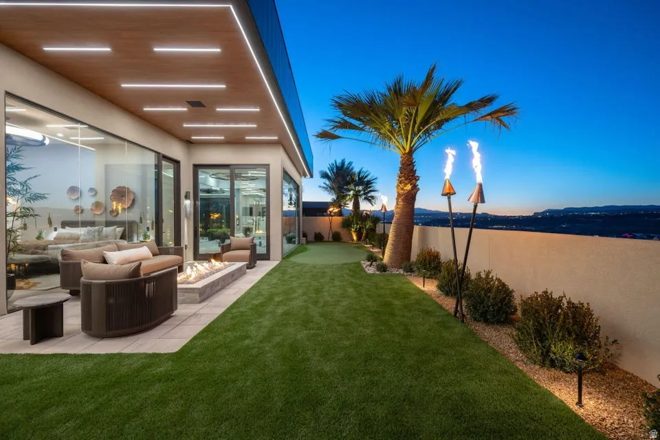 Outdoor living space featuring an expansive patio, built-in fire pit, artificial turf, and mature landscaping
