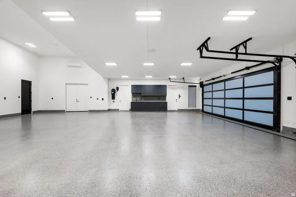 Spacious garage featuring a glass-paneled sectional door, light gray epoxy flooring, built-in dark cabinetry with a countertop, recessed square lighting, and white walls