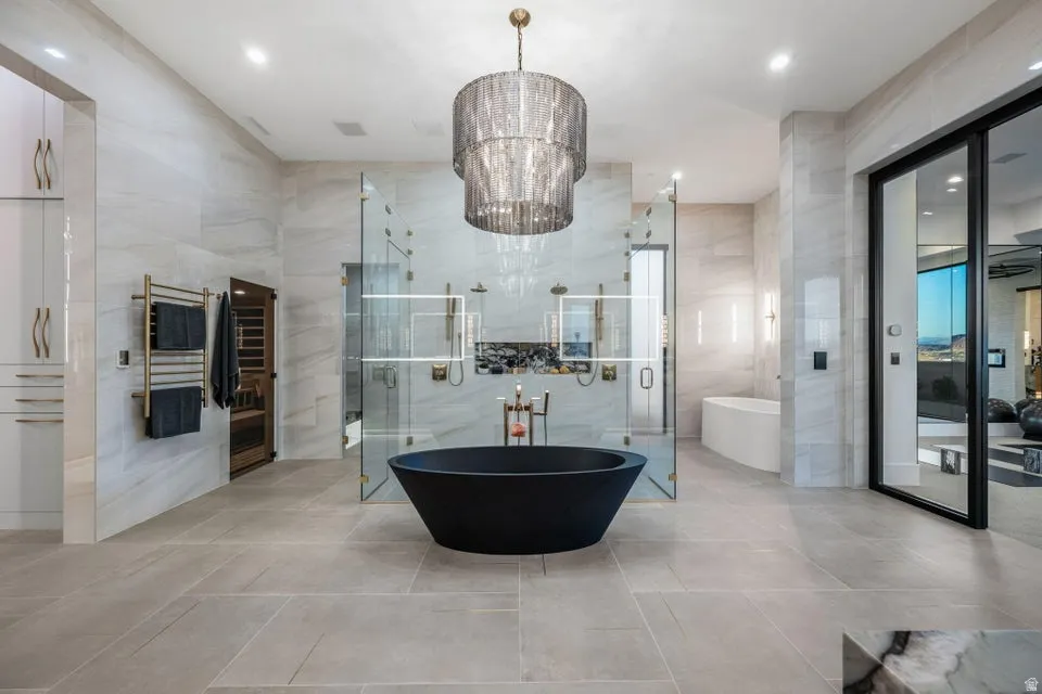 Spacious bathroom featuring a central black freestanding soaking tub, a large walk-in glass shower enclosure with multiple shower heads, a built-in sauna, light-colored large format tile flooring, and a tiered chandelier