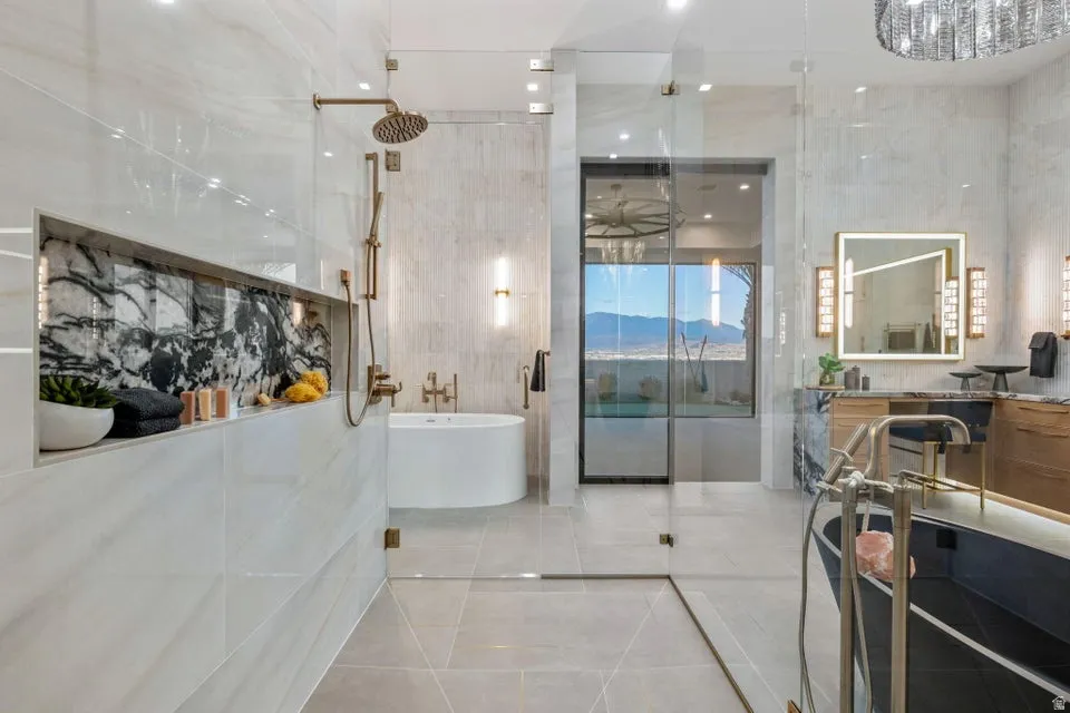 Contemporary bathroom featuring a spacious glass-enclosed shower with bronze fixtures, a built-in shelf with dark veined stone accent, a freestanding soaking tub, a dual vanity with illuminated mirror, and large format tile flooring