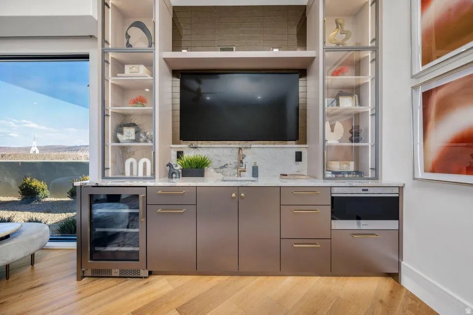 Integrated media console with a built-in television, open shelving with glass fronts, a beverage refrigerator, a built-in microwave, and a wet bar with a sink and faucet
