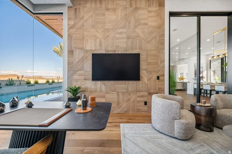 Floor-to-ceiling glass wall, wood-finish flooring, patterned wood wall paneling, sliding glass door, and a built-in entertainment area