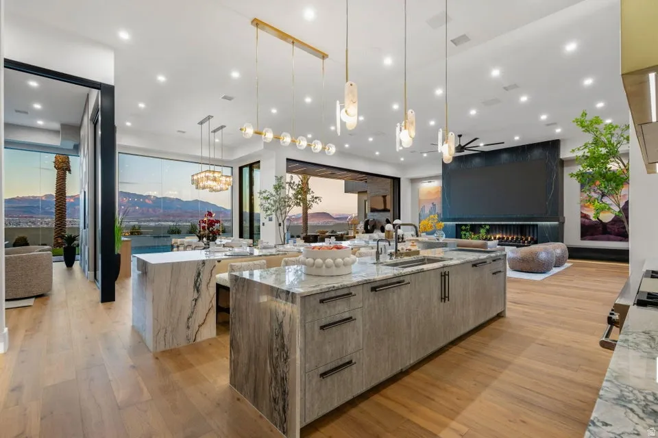 Gourmet kitchen featuring a large waterfall island with integrated sink, wood-finish flooring, recessed lighting, and a modern linear chandelier