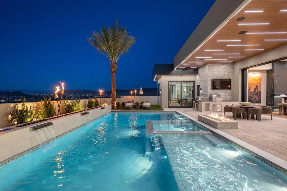 Resort-style pool area featuring integrated water features, an elevated fire pit, and an outdoor kitchen with stone accents