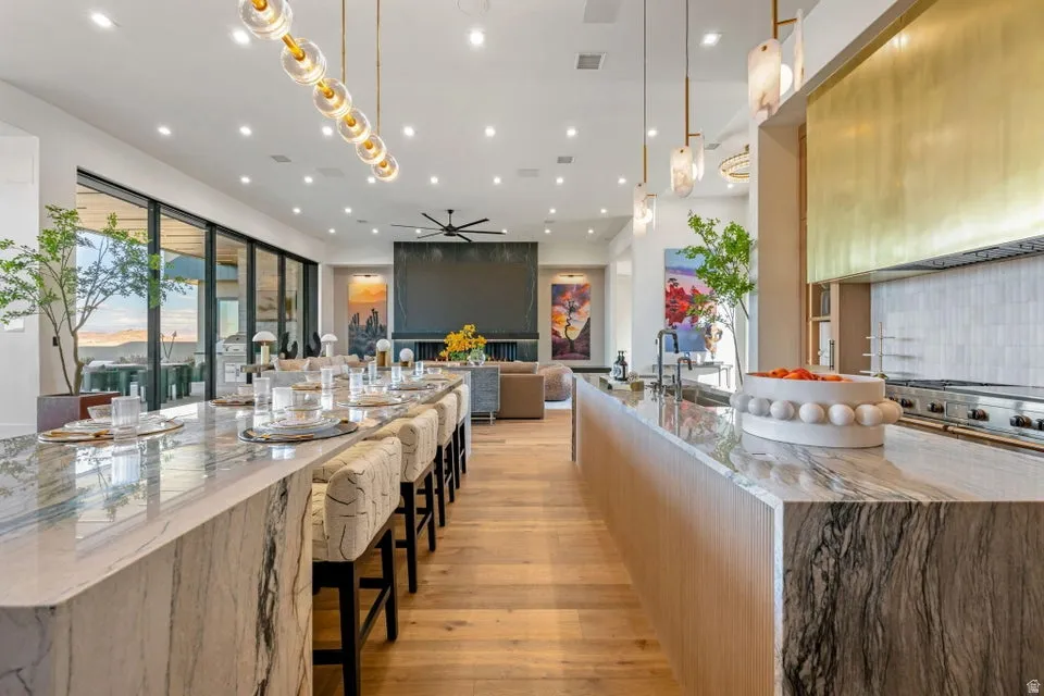 Expansive kitchen featuring two large waterfall islands with stone countertops, a gold-toned range hood, and a wall of glass sliding doors