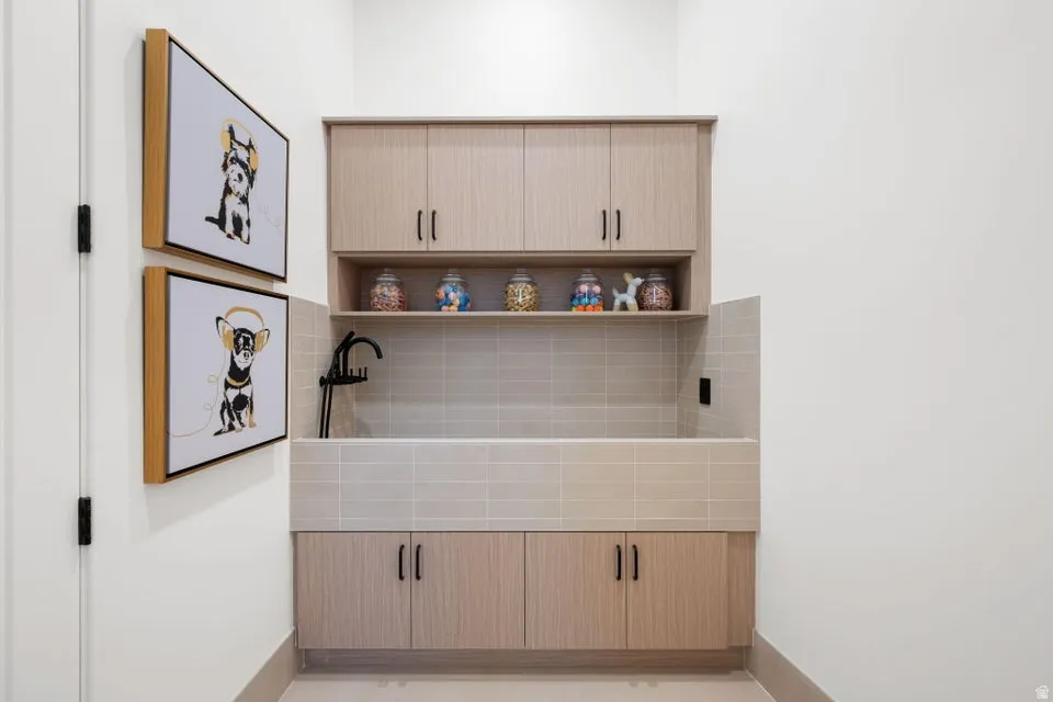 Dedicated utility space featuring a built-in wash basin with tiled surround, light wood-finish cabinetry, an open display shelf, and a matte black faucet
