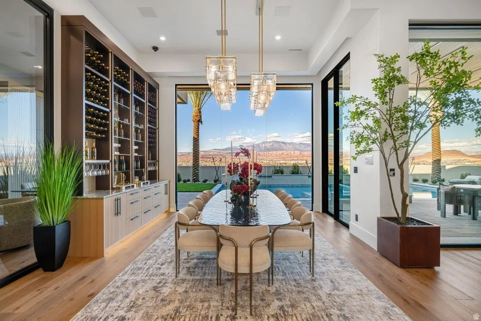Spacious dining area featuring wood-finish flooring, a full-height built-in wine storage system, and two contemporary chandeliers