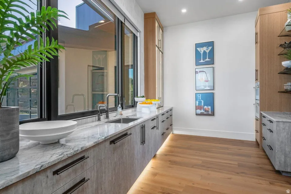 Sleek kitchen area featuring a large picture window, stone countertop, integrated sink with modern faucet, under-cabinet lighting, and wood-finish flooring