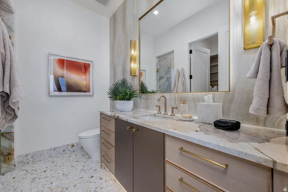 Bathroom featuring a floating vanity with a stone countertop, an undermount sink, and brass hardware