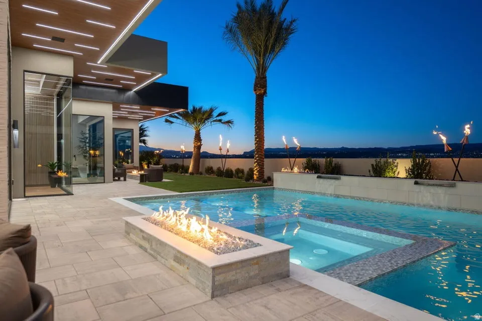 Expansive outdoor living area featuring a swimming pool with integrated spa, a linear fire feature, paver patio, and a grass lawn