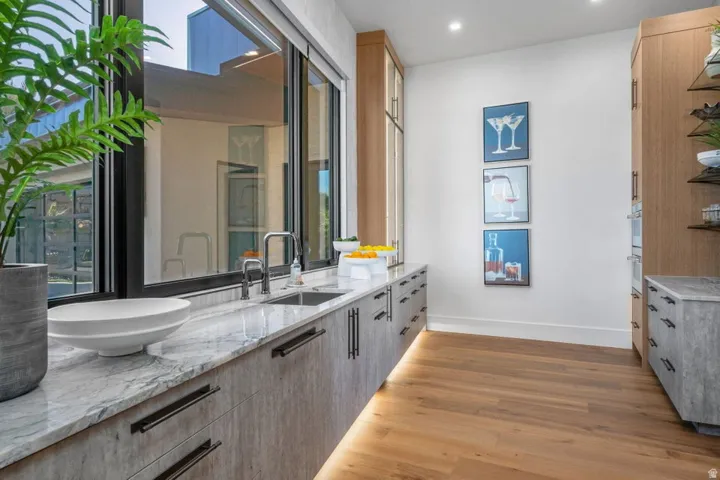 Sleek kitchen area featuring a large picture window, stone countertop, integrated sink with modern faucet, under-cabinet lighting, and wood-finish flooring