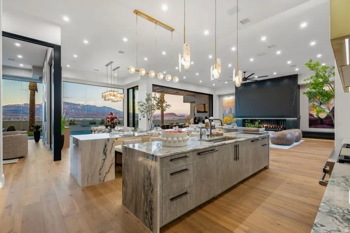 Gourmet kitchen featuring a large waterfall island with integrated sink, wood-finish flooring, recessed lighting, and a modern linear chandelier