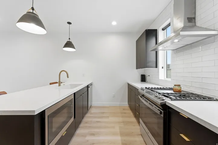 Kitchen featuring stainless steel appliances, dark cabinetry with gold-tone hardware, white countertops, and light wood-finish flooring