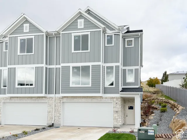 Multi-story exterior featuring board-and-batten siding, horizontal lap siding, stone veneer accents, multi-pane windows, and a concrete driveway leading to two garages