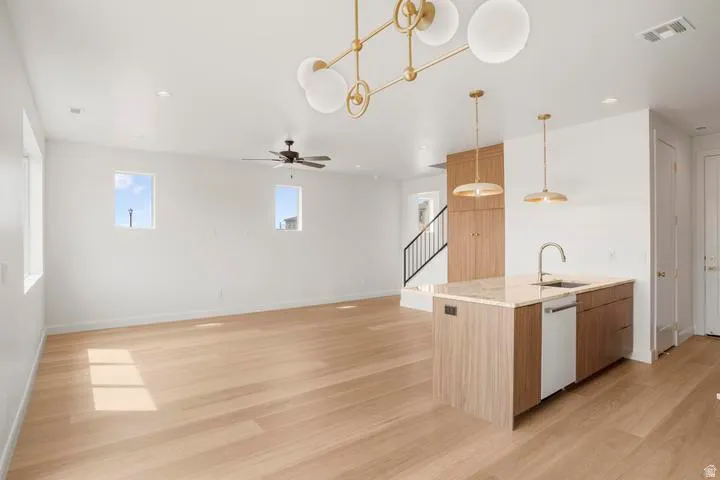 Open-concept living space featuring wood-finish flooring, a contemporary kitchen island with a built-in sink and dishwasher, and modern pendant lighting