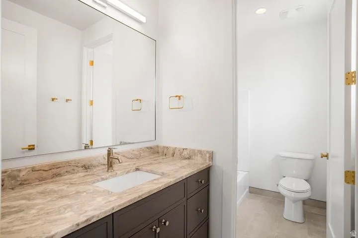Bathroom featuring a vanity with a light-toned stone countertop, integrated rectangular sink, and dark wood-finish cabinetry with brass hardware